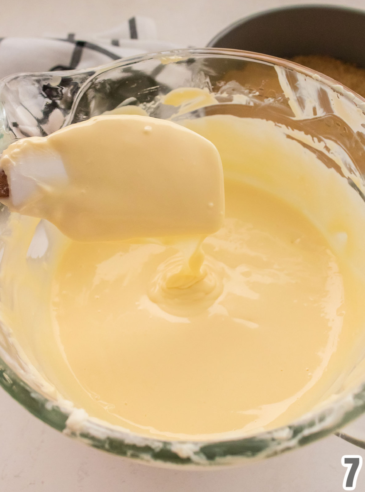 A glass bowl sitting on a white table filled with the cheesecake Cream Cheese mixture.