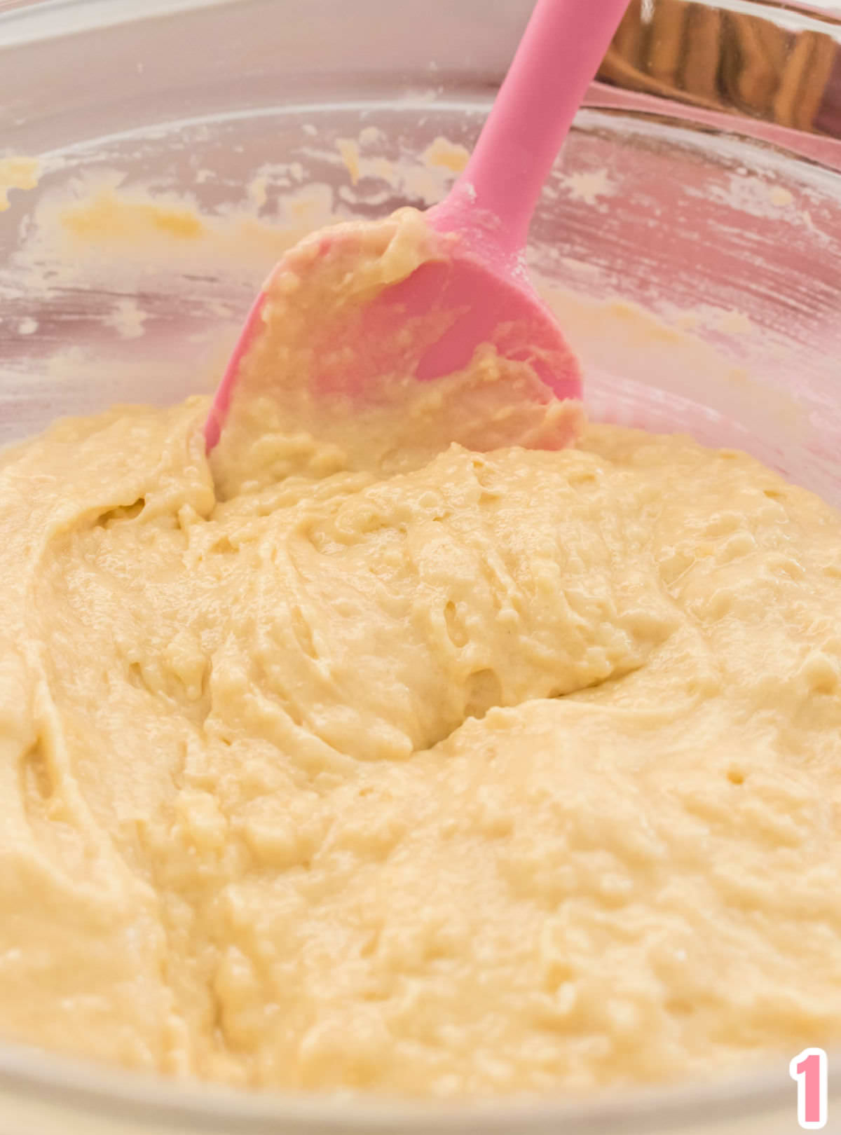Close up image of the cake batter in a glass bowl with a pink spatula.