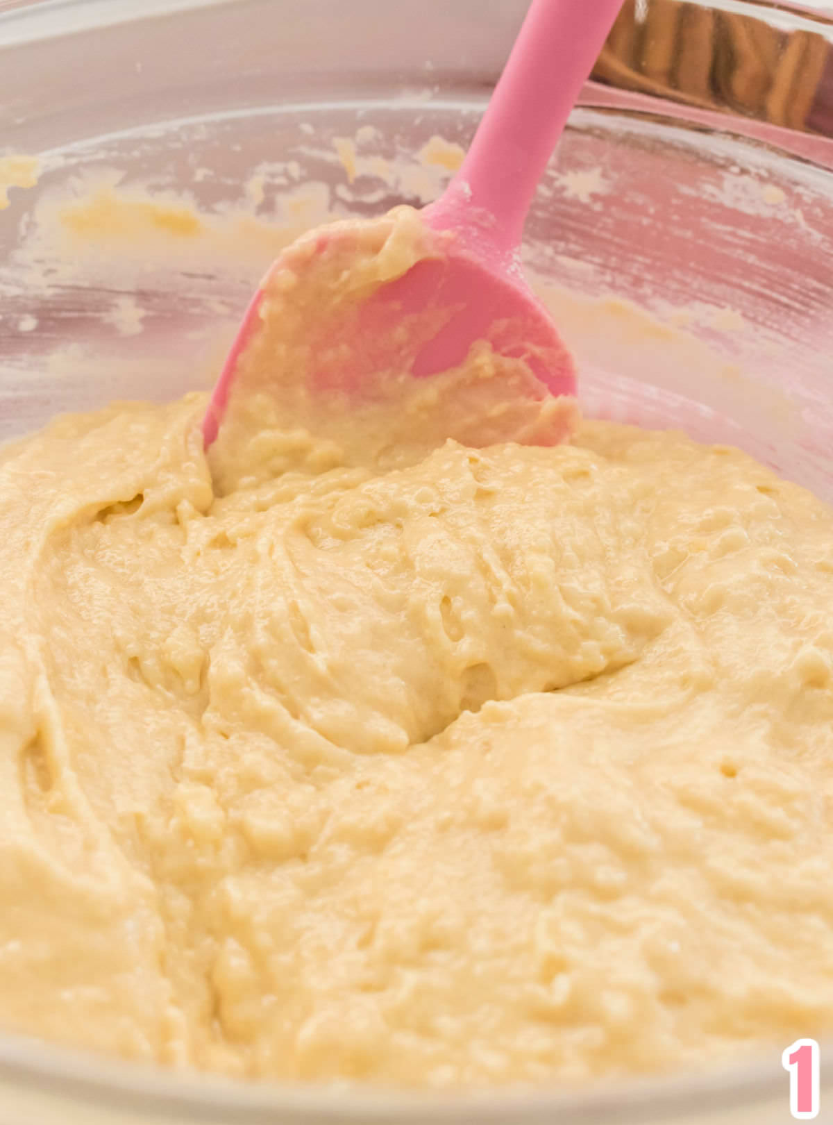 Close up image of the cake batter in a glass bowl with a pink spatula.