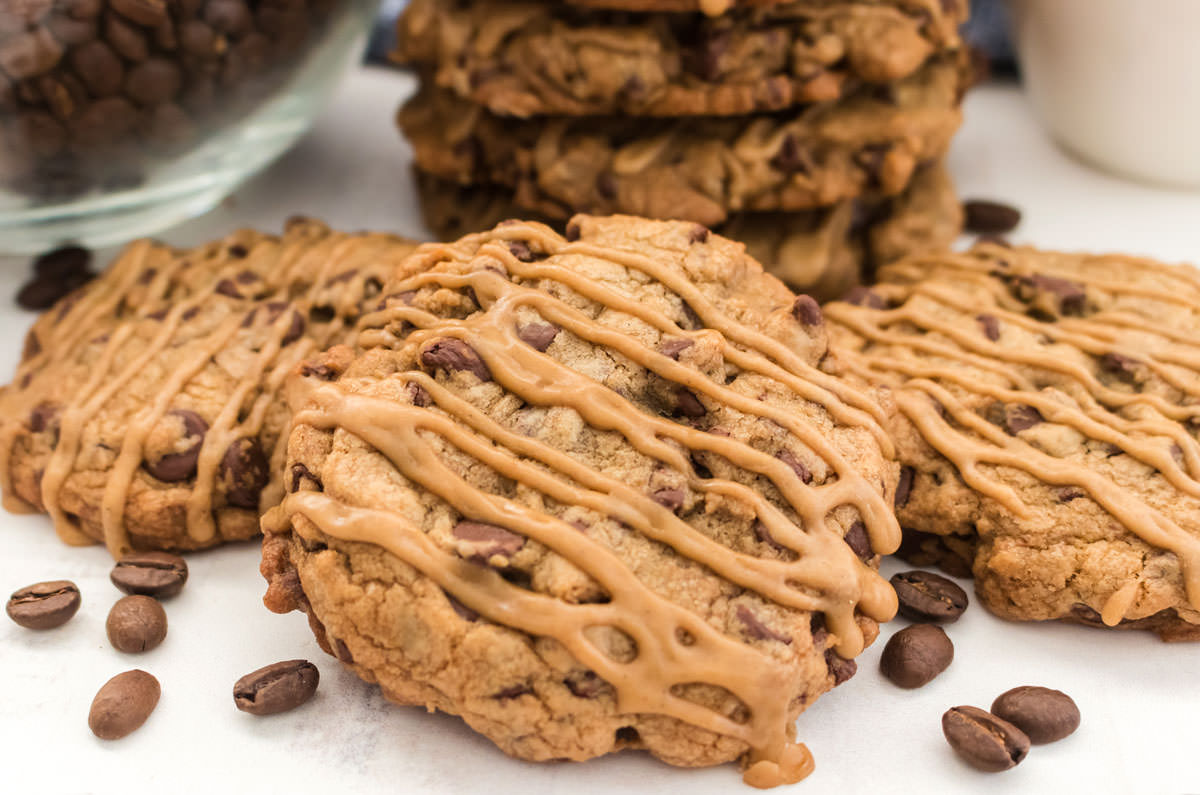 Close up on a stack of three Coffee Chocolate Chip Cookies laying on a white table next to a glass bowl filled with coffee beans.