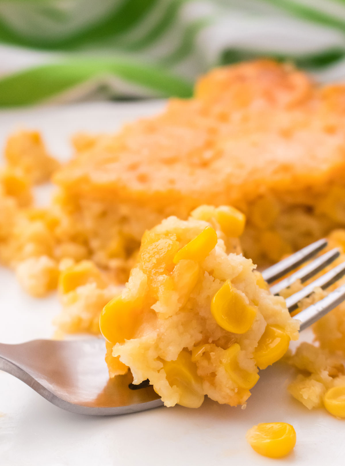 Closeup on a single serving of Corn Casserole on a white dinner plate with a piece resting on a fork.