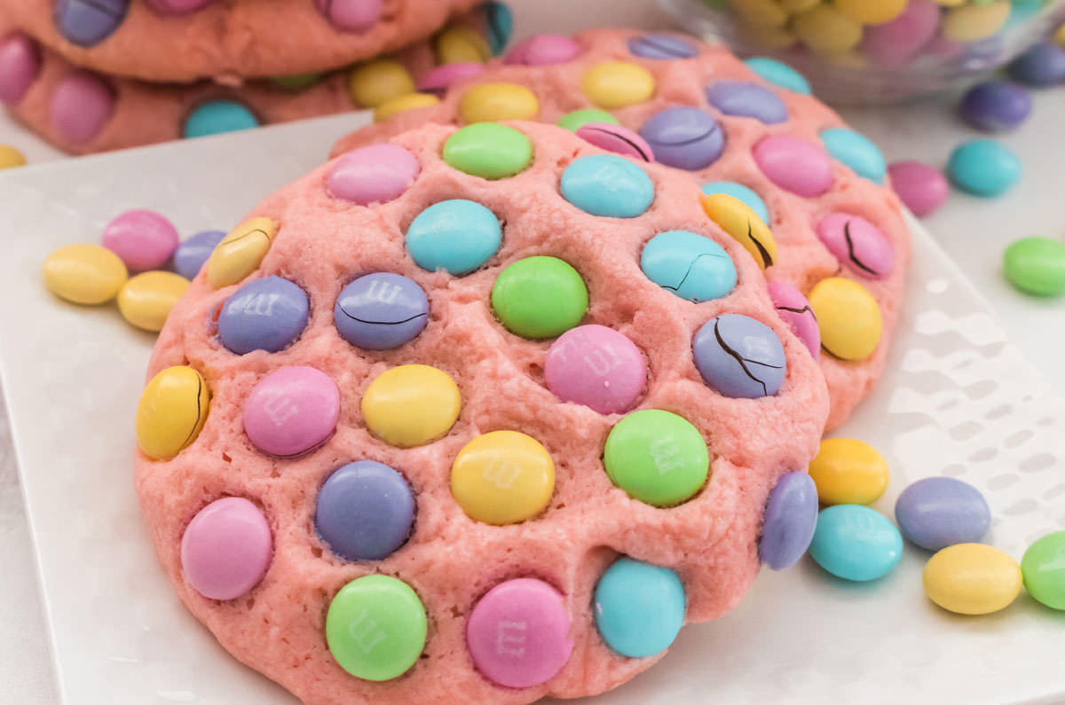 Two pink M&M's cookies sitting on a white dessert plate.