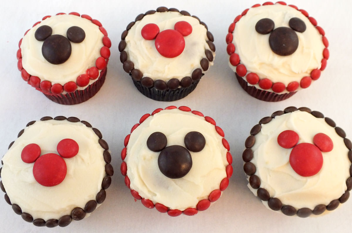 Six cupcakes decorated with M&M's sitting on a white table.