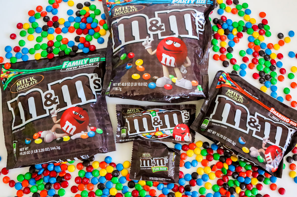 The most popular-sized bags of M&M's laying on a white table surrounded by colored M&M's.