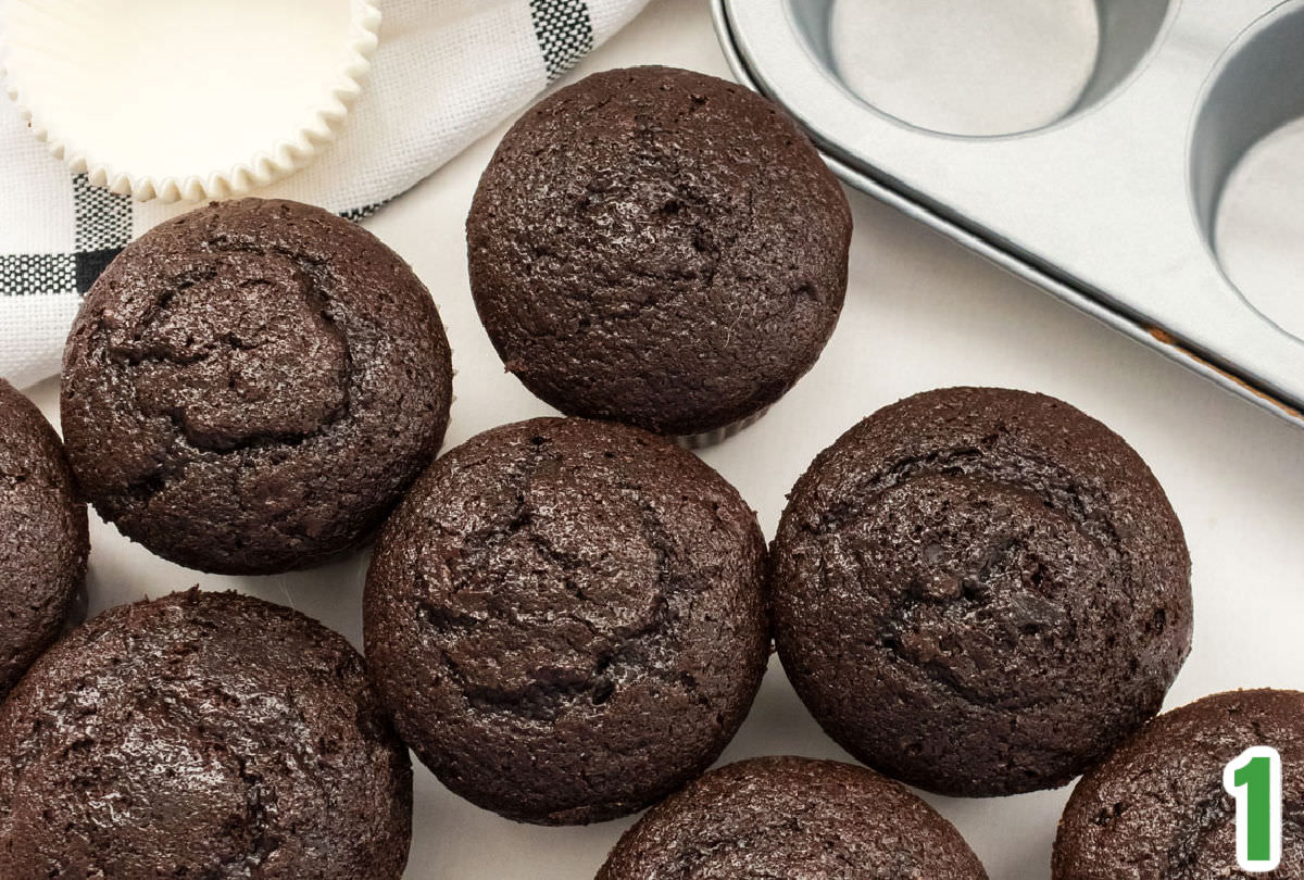 Closeup on eight chocolate cupcakes sitting on a white table.