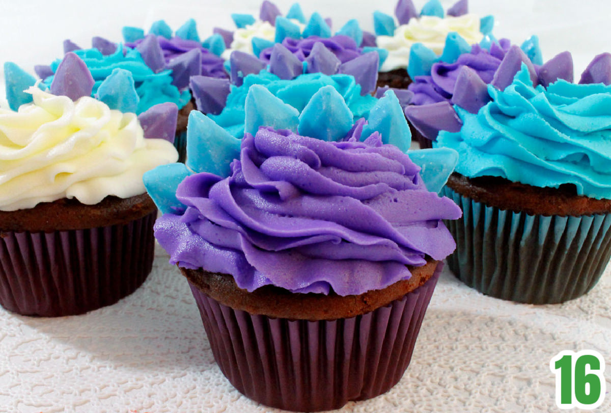 Closeup on nine Dinosaur Cupcakes sitting on a white table cloth in front of a white background.