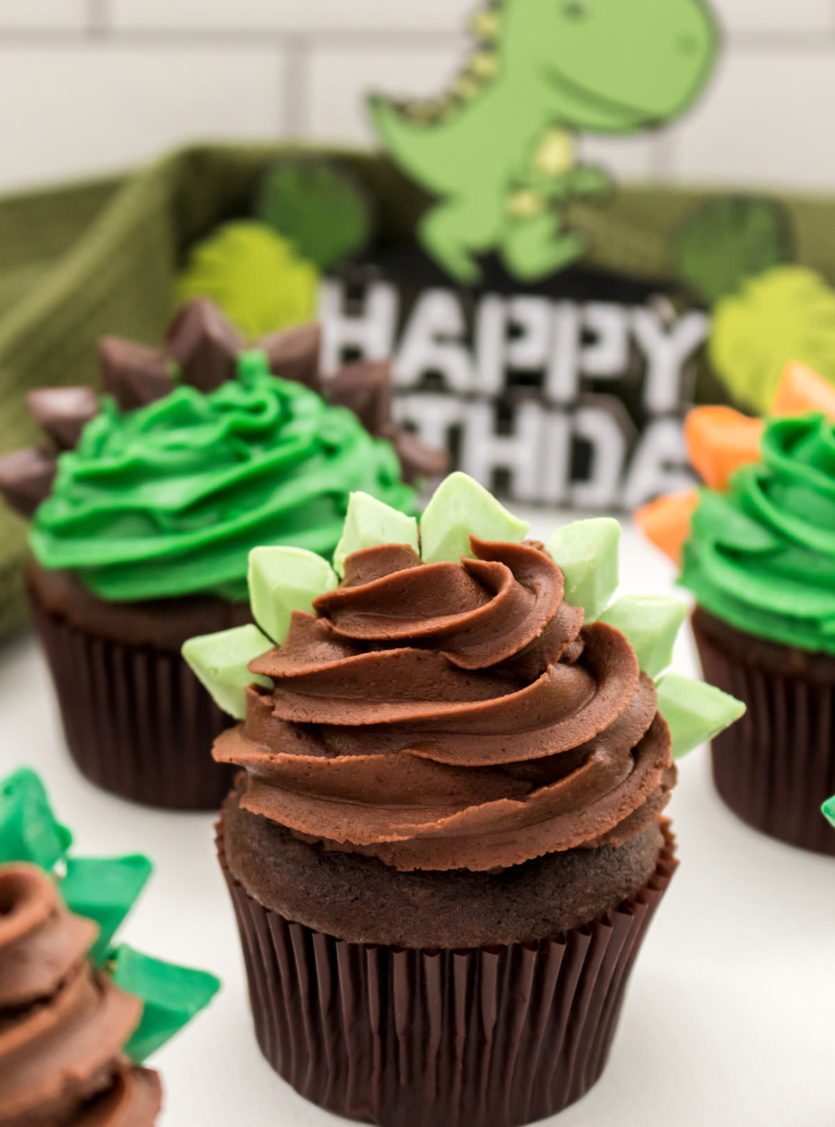 Closeup on a Dinosaur Cupcake with chocolate frosting and stegosaurus spikes with other cupcakes in the background.