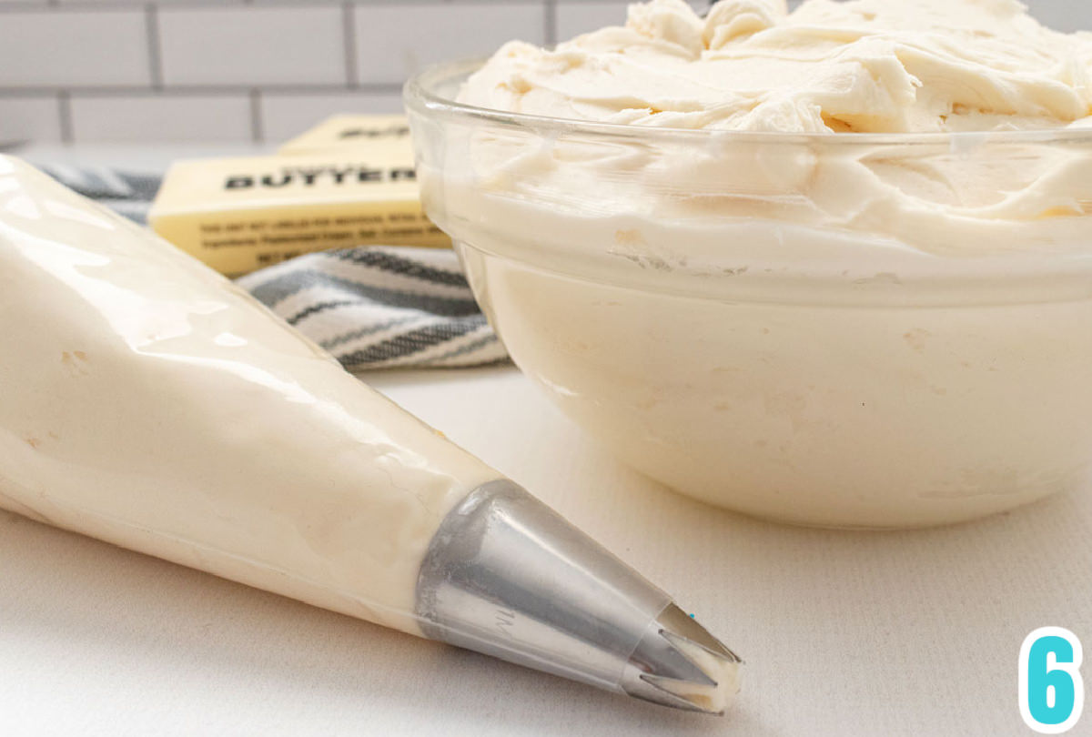 Close up on a glass bowl filled with Buttercream Frosting sitting next to a decorating bag filled with buttercream frosting.