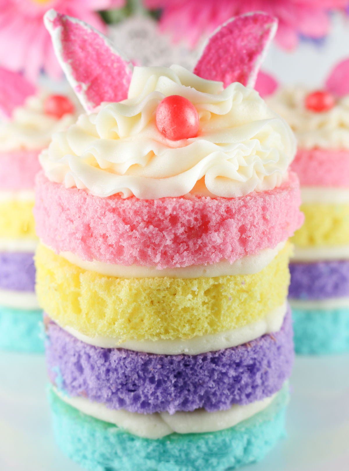 Closeup on an Easter Bunny Mini Cake sitting on a white surface in front of two other bunny cakes.