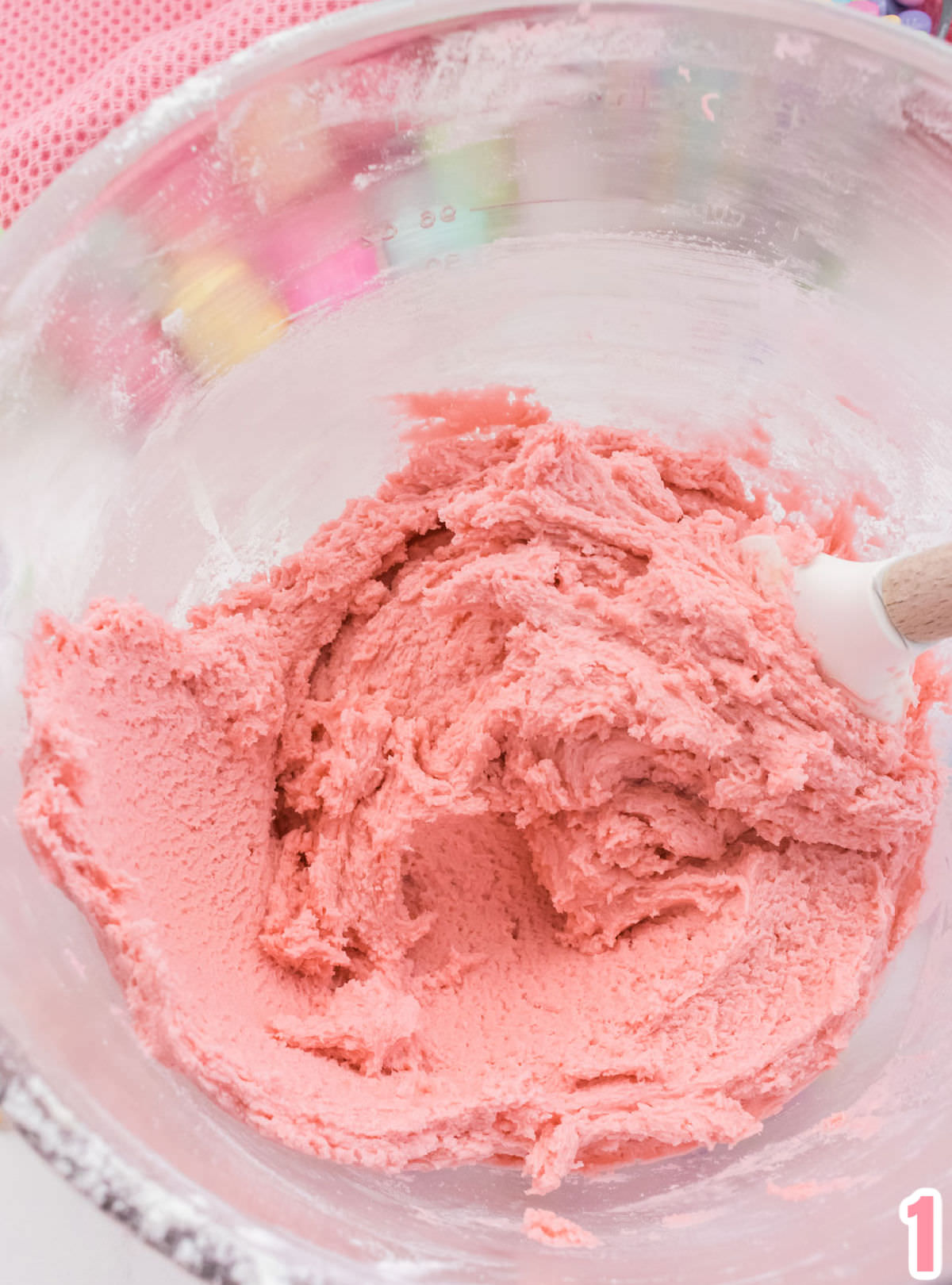 Closeup on a glass mixing bowl filled with pink sugar cookie dough.