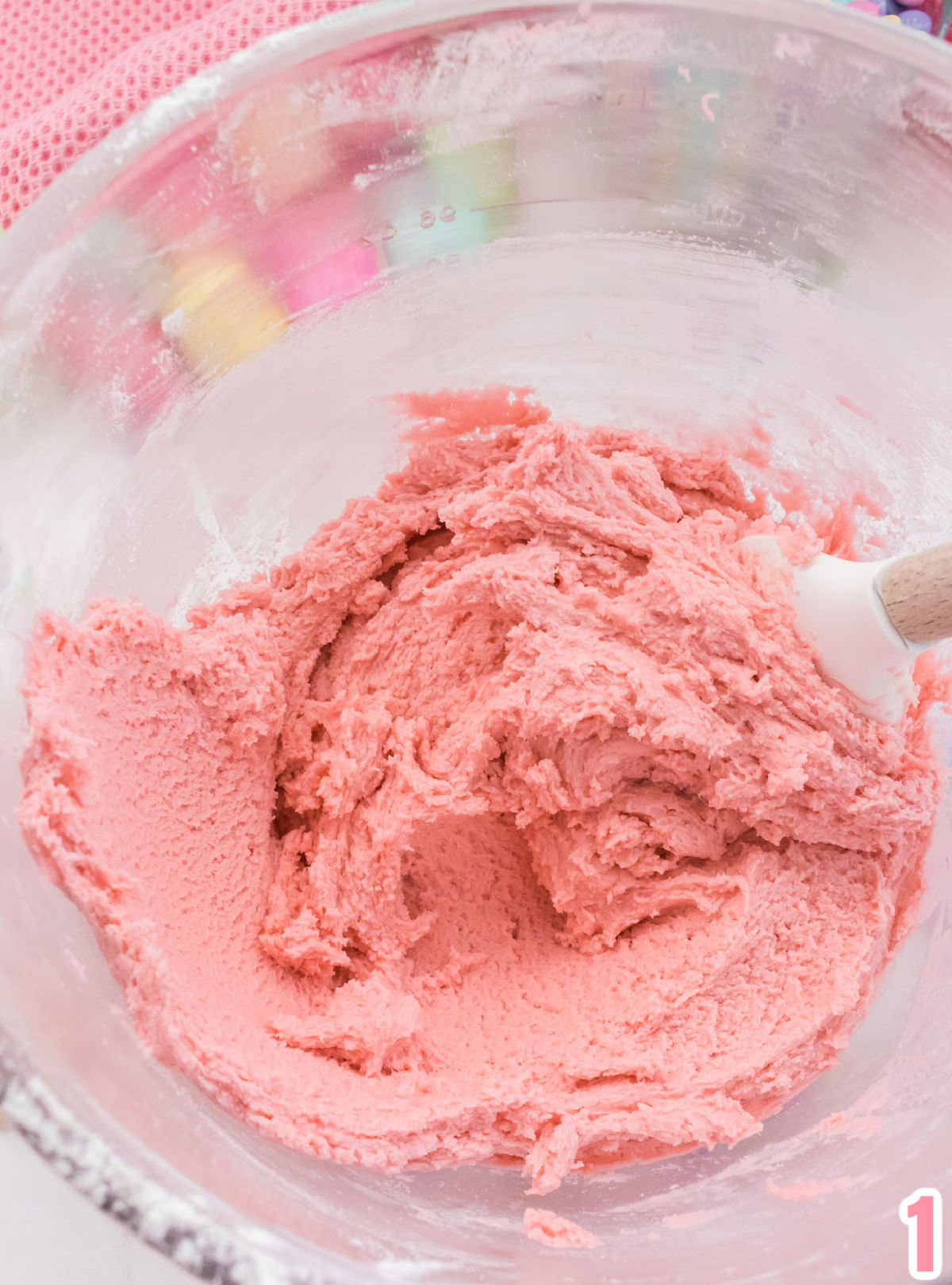 Closeup on a glass mixing bowl filled with pink sugar cookie dough.