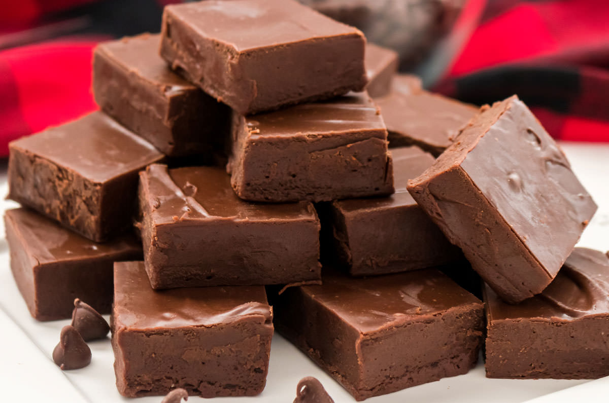 Closeup on a white plate filled with stacks of Easy Chocolate Fudge sitting in front of a red buffalo check cloth.