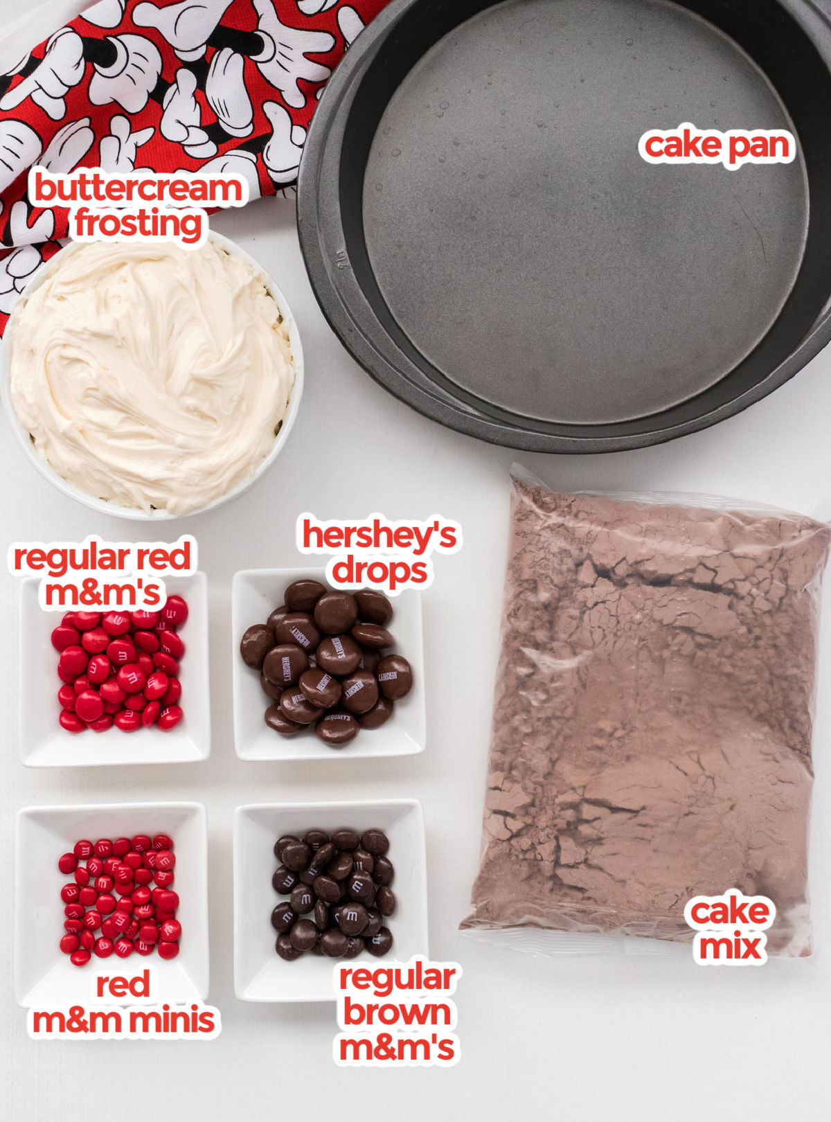 All the ingredients you will need to make an Easy Mickey Mouse Cake including cake mix, cake pans, buttercream frosting, Hershey's Chocolate Drops, Regular M&M's and M&M Minis.