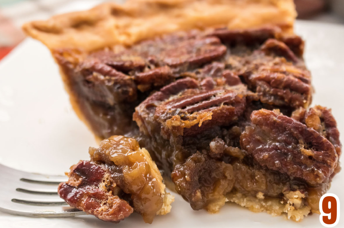 Piece of Pecan Pie on a white plate with a bite on a fork.