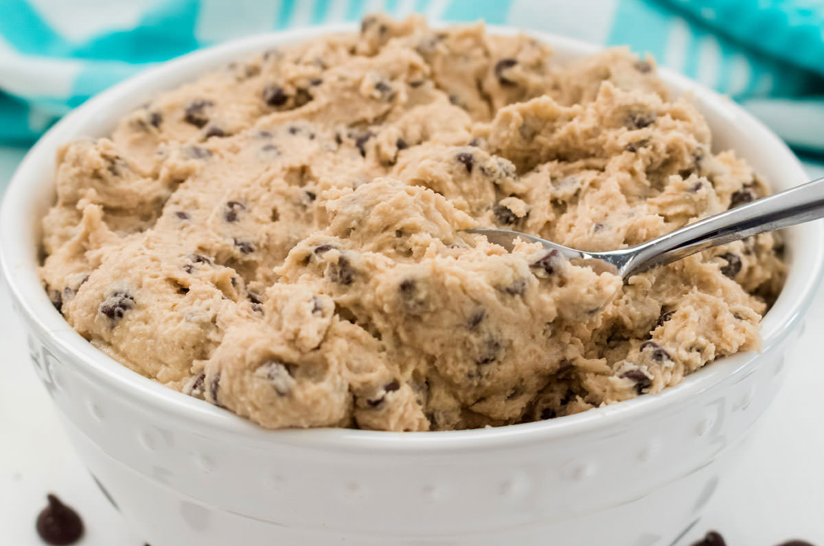 Closeup on a white bowl filled with Edible Cookie Dough with a spoon in it.