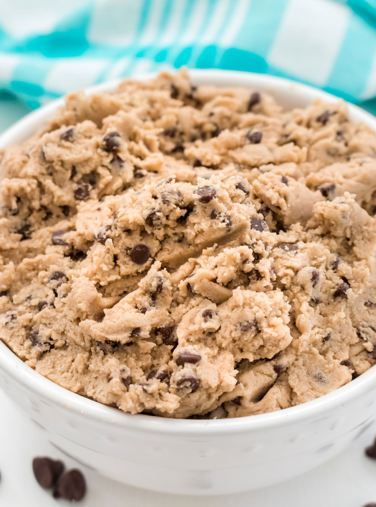 Closeup on a white bowl filled with Edible Cookie Dough sitting on a white table in front of an aqua table linen.