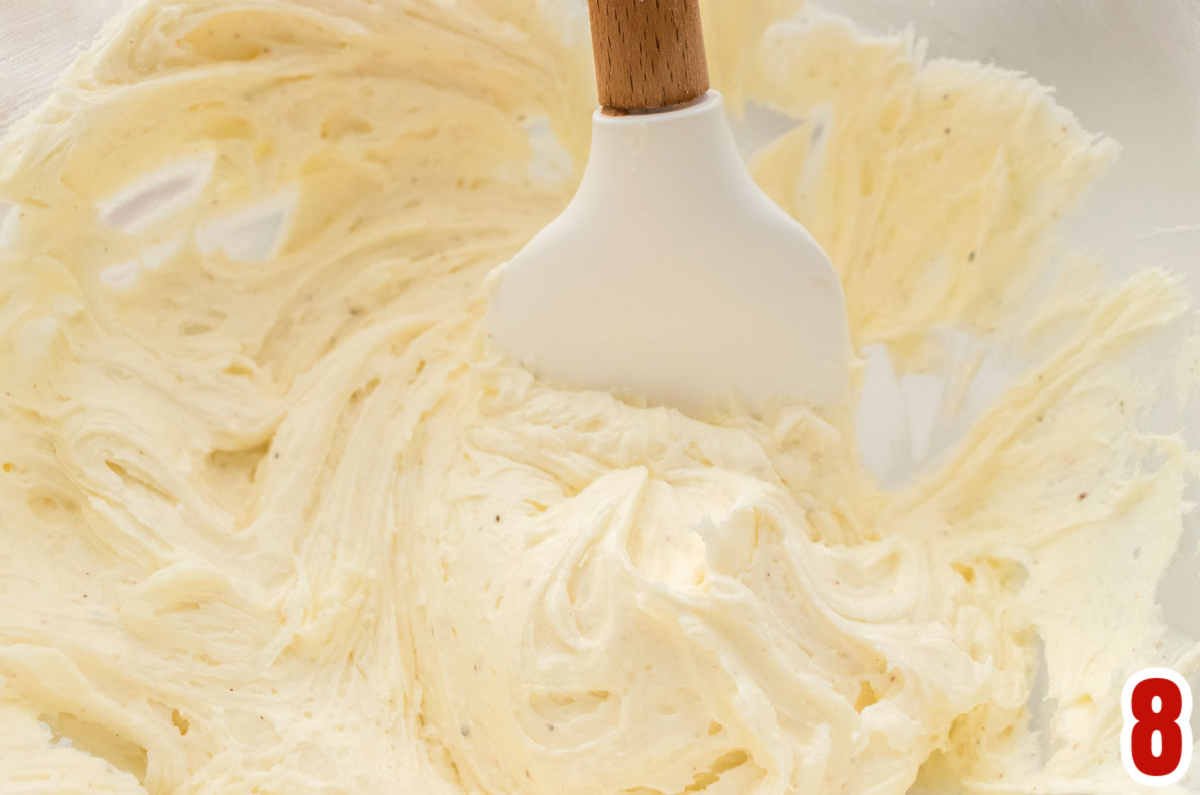 Closeup on a clear mixing bowl filled with Eggnog Frosting and a white spatula.