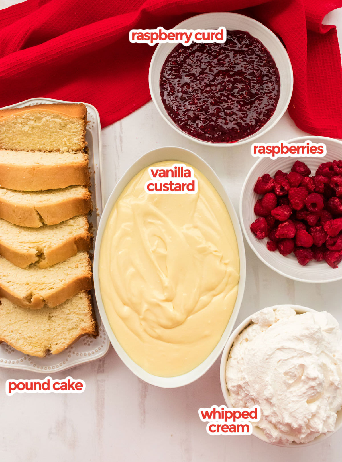 All the ingredients needed to make English Trifle including Pound Cake, Vanilla Custard, Raspberry Curd, Fresh Raspberries, and Whipped Cream.