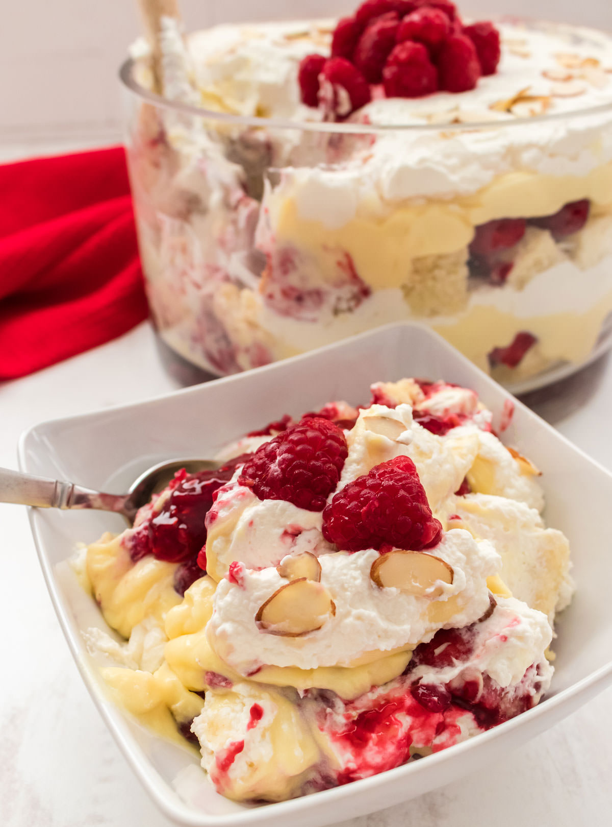A white bowl filled with a serving of English Trifle sitting in front of a round glass bowl filled with the rest of the English Trifle.