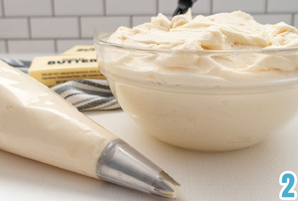 Closeup on a glass bowl filled with buttercream frosting sitting next to a decorator bag filled with buttercream frosting.