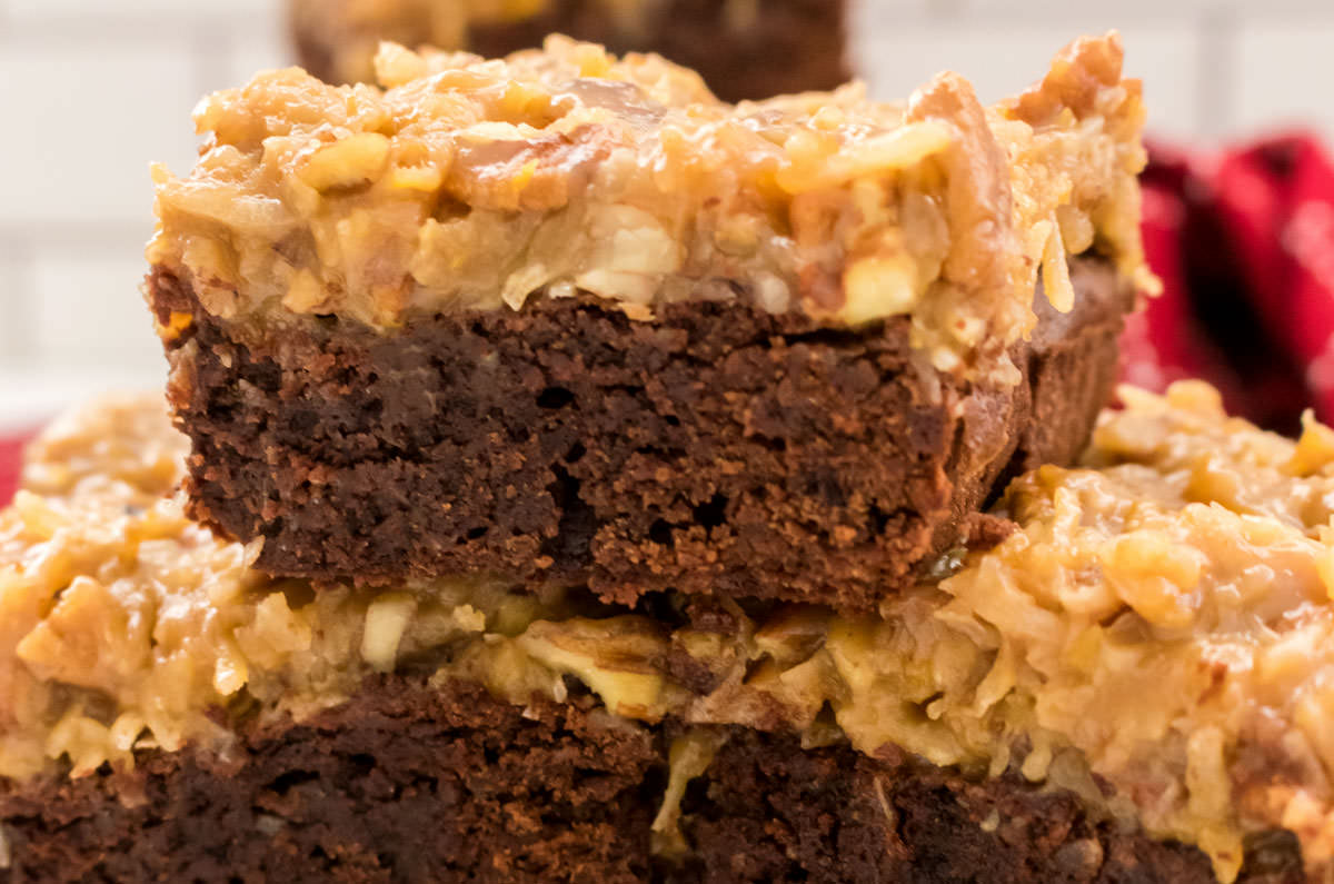Closeup on three German Chocolate Brownies sitting in a stack in front of the a red kitchen towel.