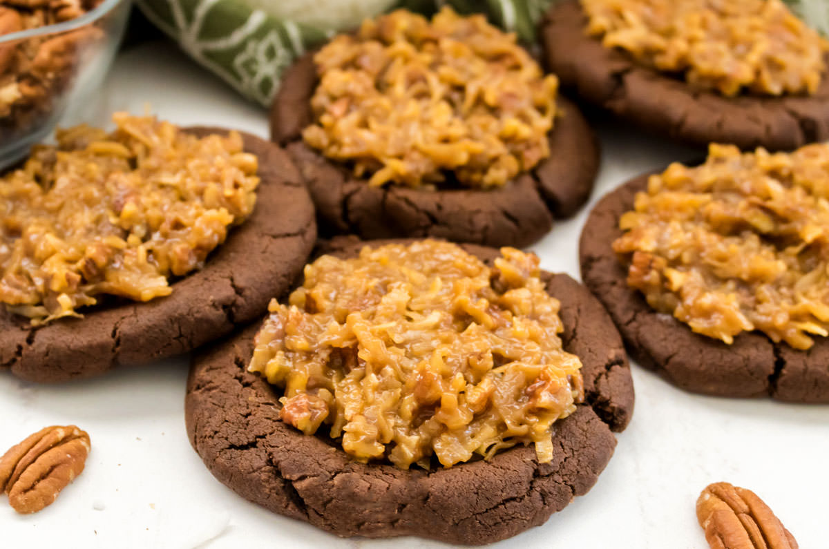 Closeup on a batch of German Chocolate Cookies sitting on a white table surrounded by pecans.