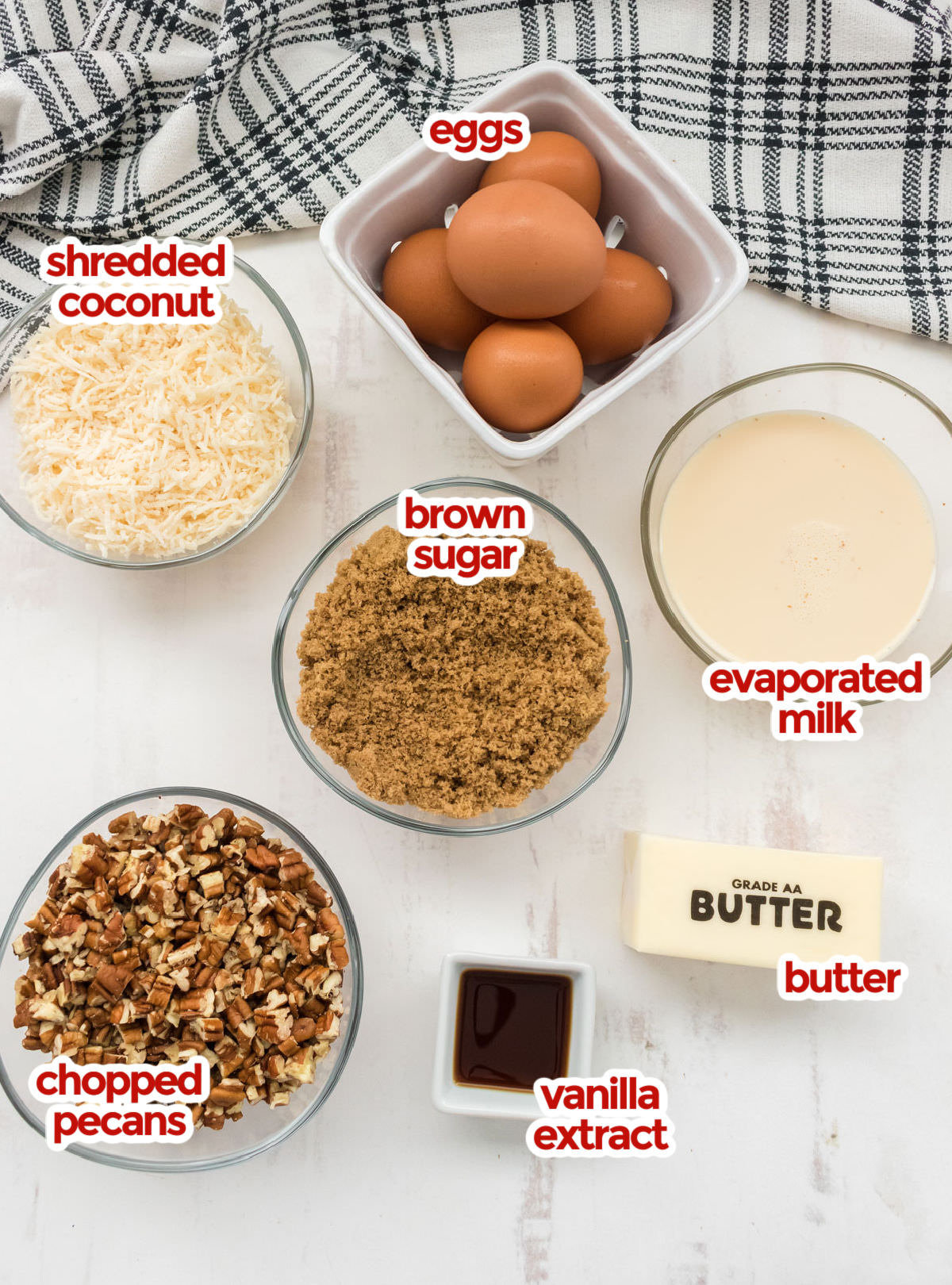 All the ingredients you will need to make The Best German Chocolate Cake Frosting including Butter, Eggs, Evaporated Milk, Brown Sugar, Vanilla Extract, Shredded Coconut and Chopped Pecans.