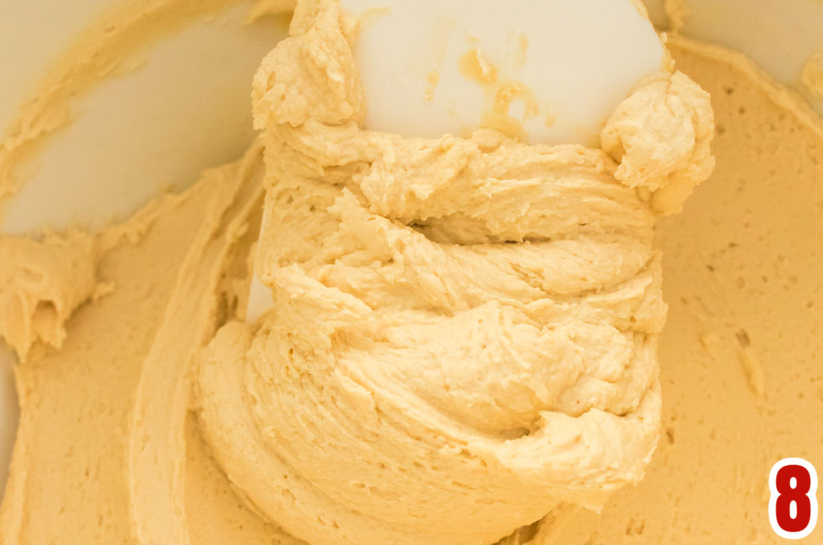 Closeup on a white mixing bowl filled with Gingerbread Frosting and a white spatula.