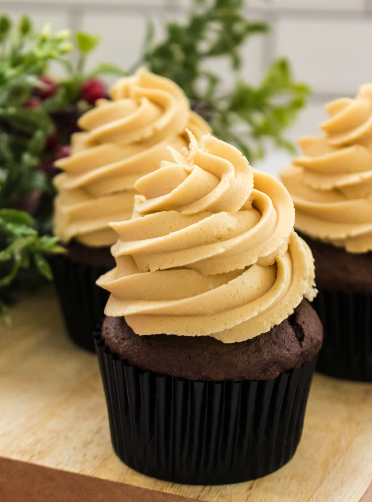 Closeup on three chocolate cupcakes topped with The Best Gingerbread Buttercream Frosting sitting on a wooden cutting board.