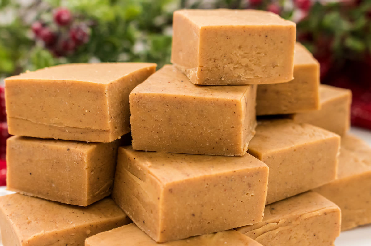 Closeup on a stack of Gingerbread Fudge pieces sitting on a white table in front of Christmas decorations.