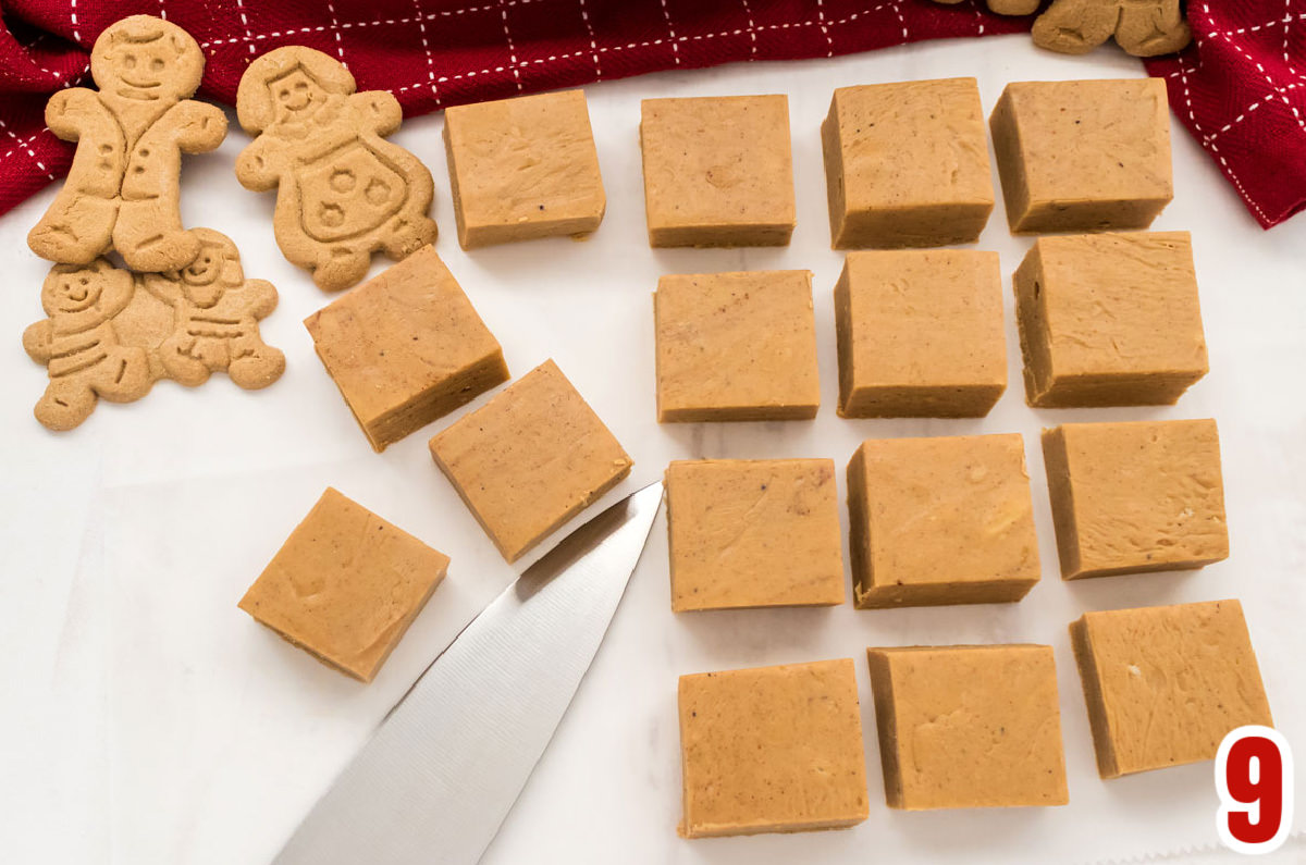Sixteen pieces of Gingerbread Fudge arranged in rows sitting next to Gingerbread cookies and a silver knife.