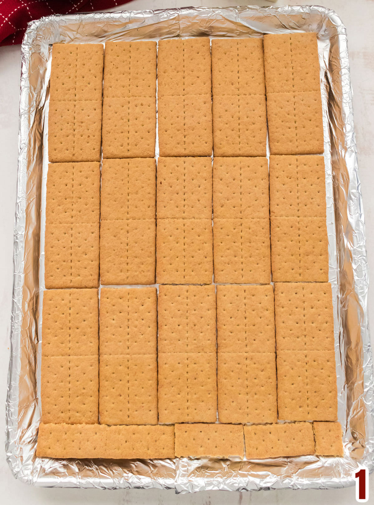 Closeup on a cookie sheet covered in aluminum foil covered with a layer of Graham Crackers.