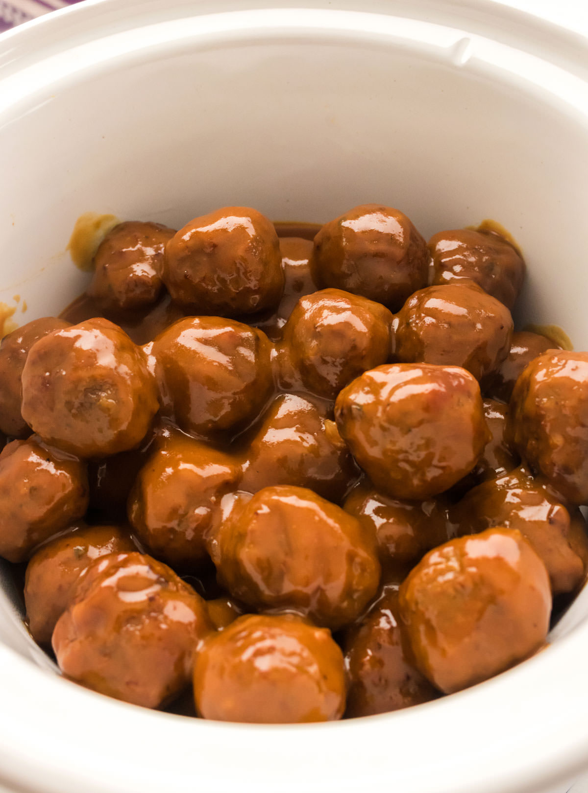 Closeup on a white Crockpot filled with Grape Jelly Meatballs.