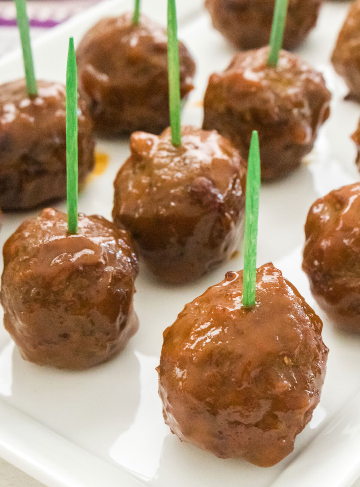 Closeup on a white serving platter filled with Grape Jelly Meatballs with toothpicks sticking out of them.