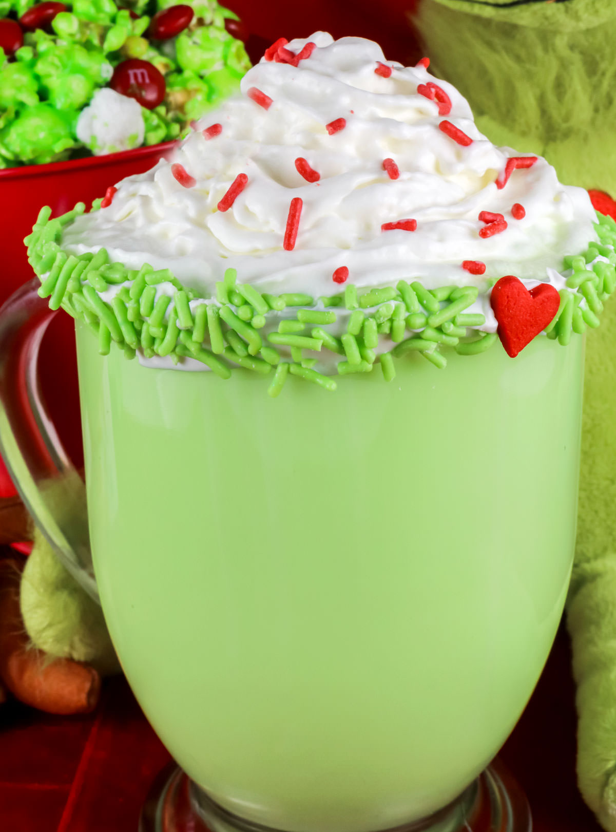 Closeup on a mug of Grinch Hot Vanilla Milk topped with Whipped Cream and red sprinkles.