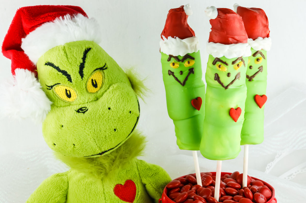 Grinch Doll face sitting next to three Grinch Marshmallow Pops.
