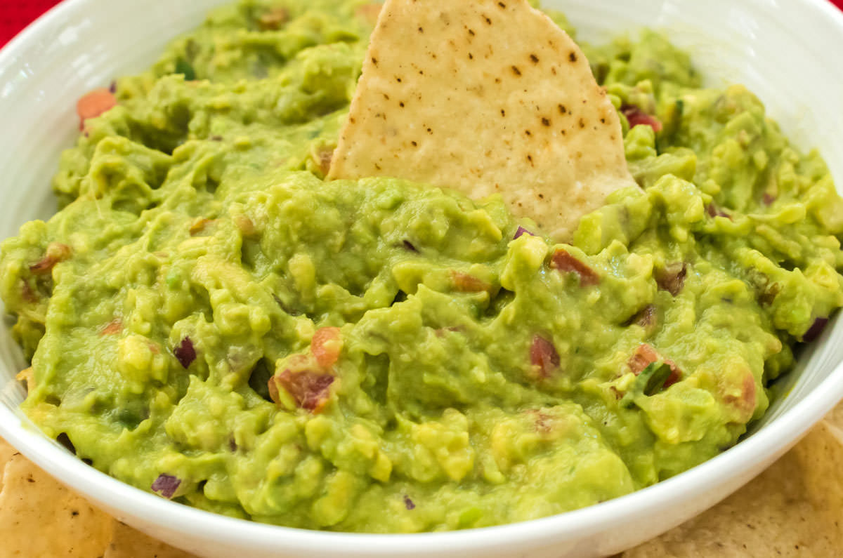 Close on a white bowl filled with homemade guacamole, a single tortilla chip.