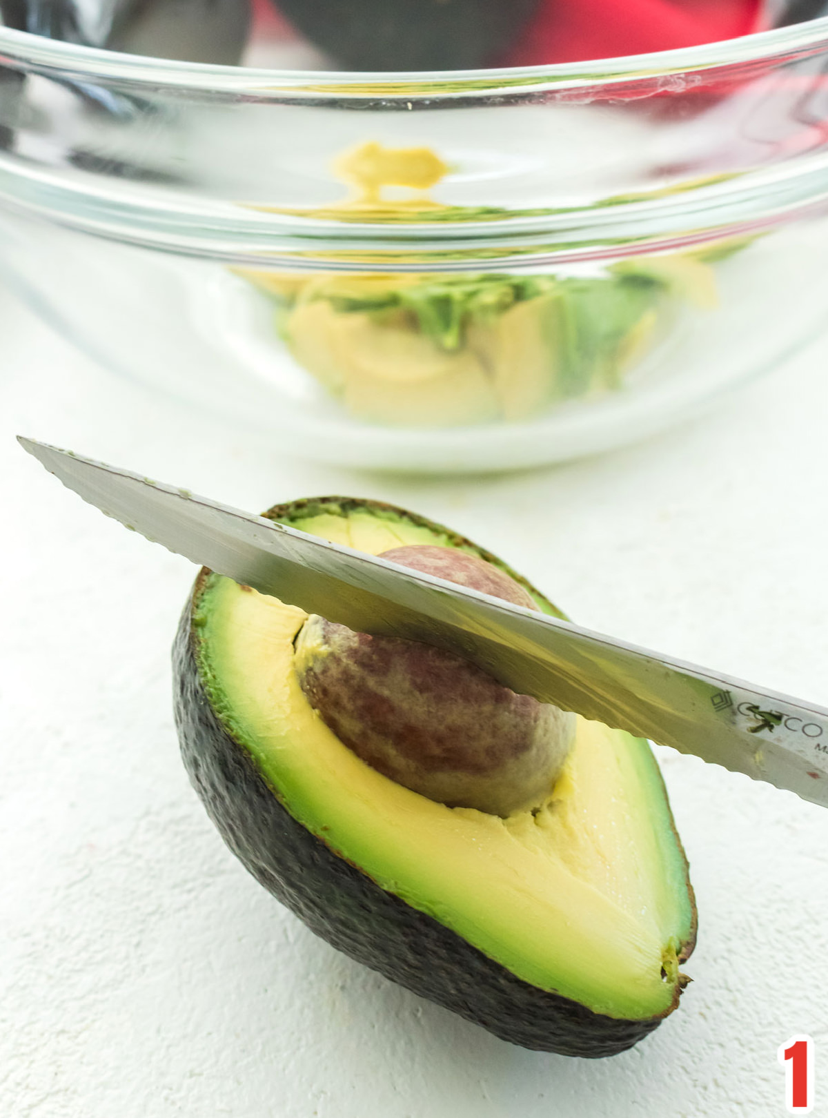 Closeup of an avocado, split in half, with a knife in the avocado pit.