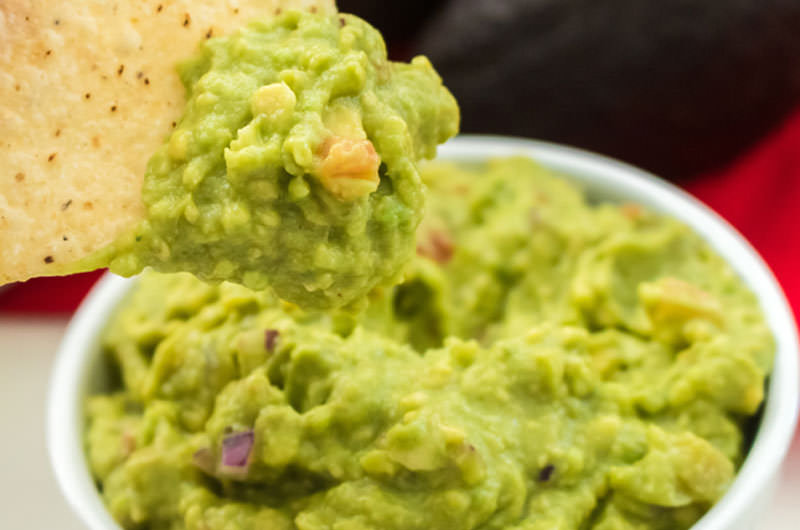 Small white ramekin filled with guacamole with a tortilla chip with guacamole on it.