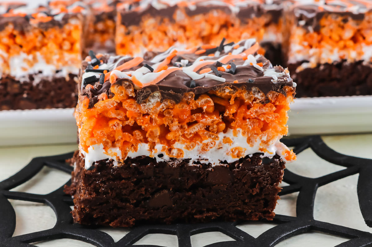 Closeup of a Halloween Brownie Rice Krispie Treat sitting on a spider web in front of a platter full of brownie bars.