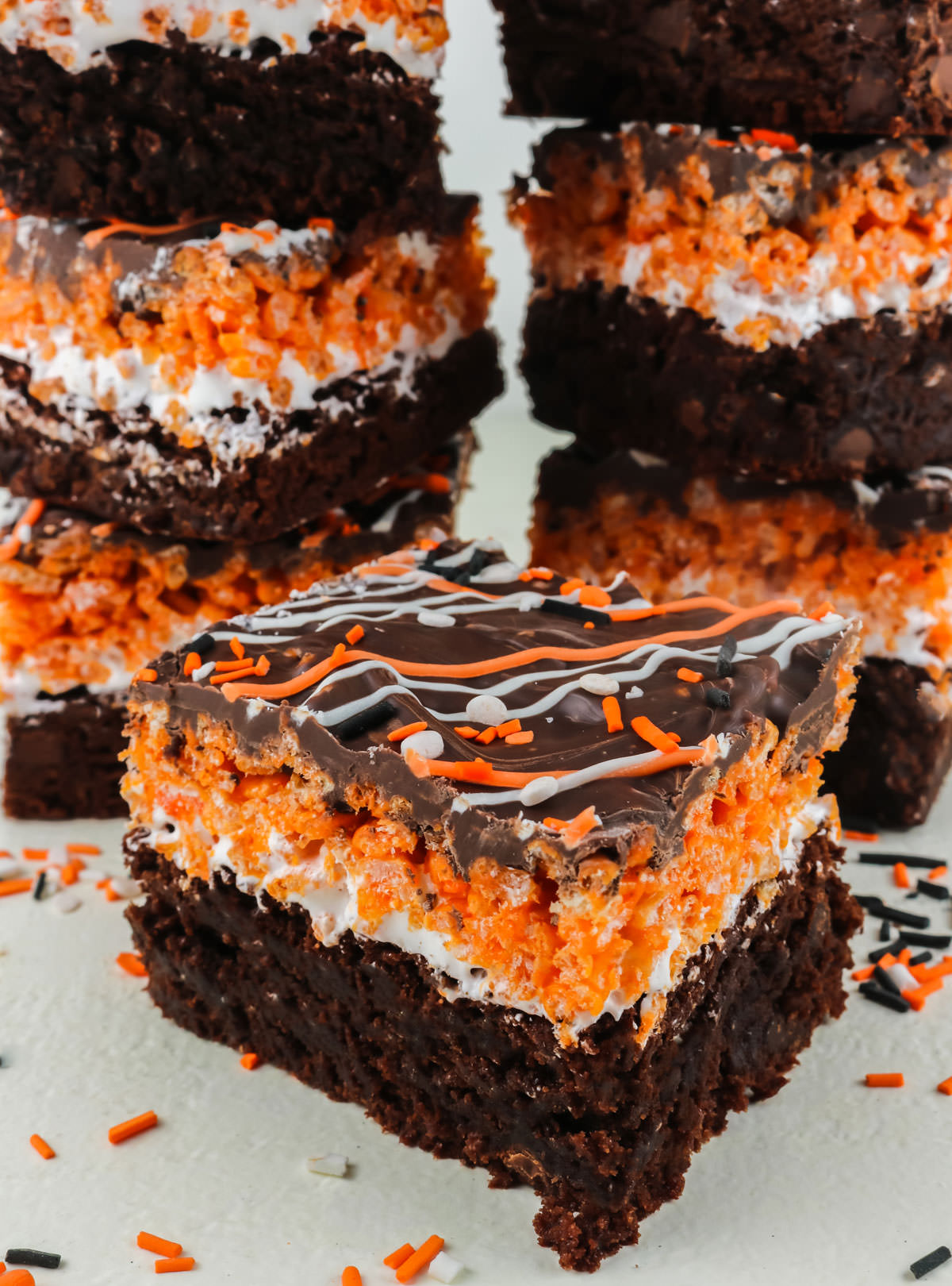 Closeup on a Halloween Brownie Rice Krispie Treat sitting on a white surface in front of stacks of other brownie bars.