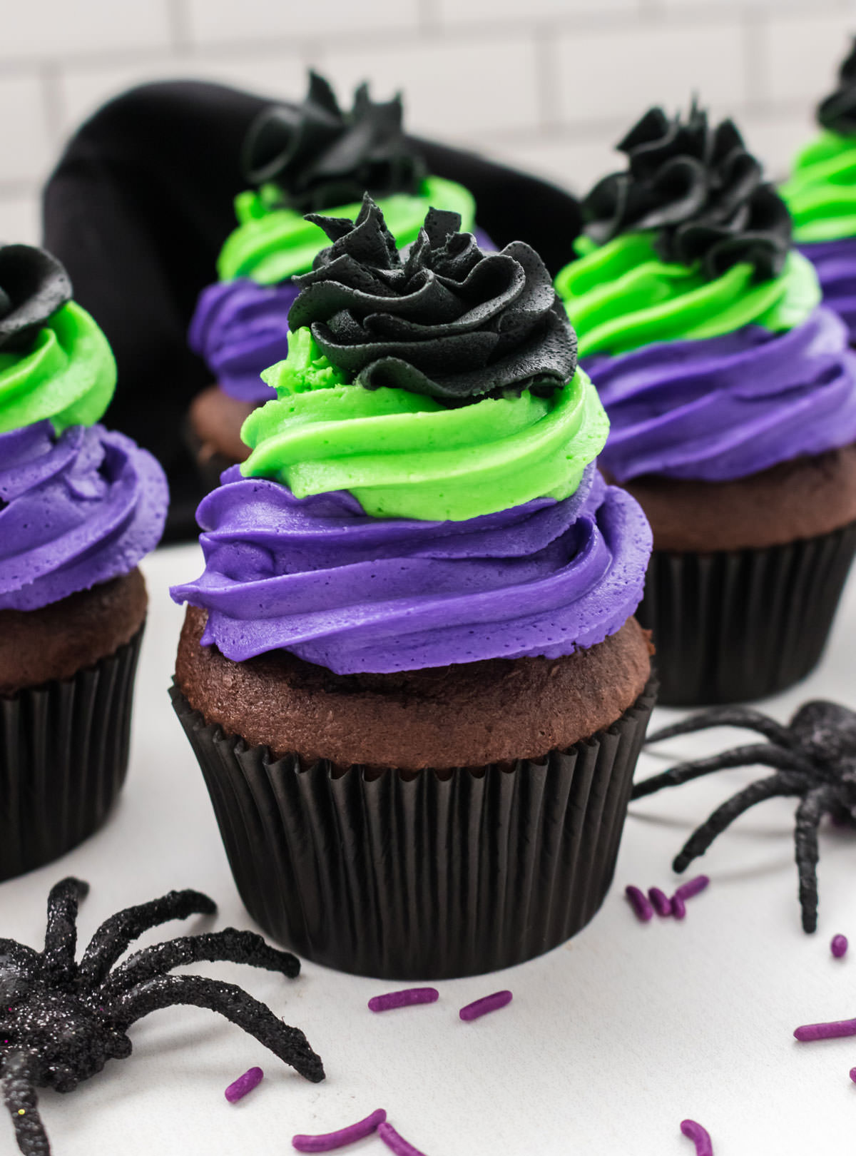 Closeup on five Bewitched Halloween Cupcakes sitting on a white table surround by toy spiders and sprinkles.