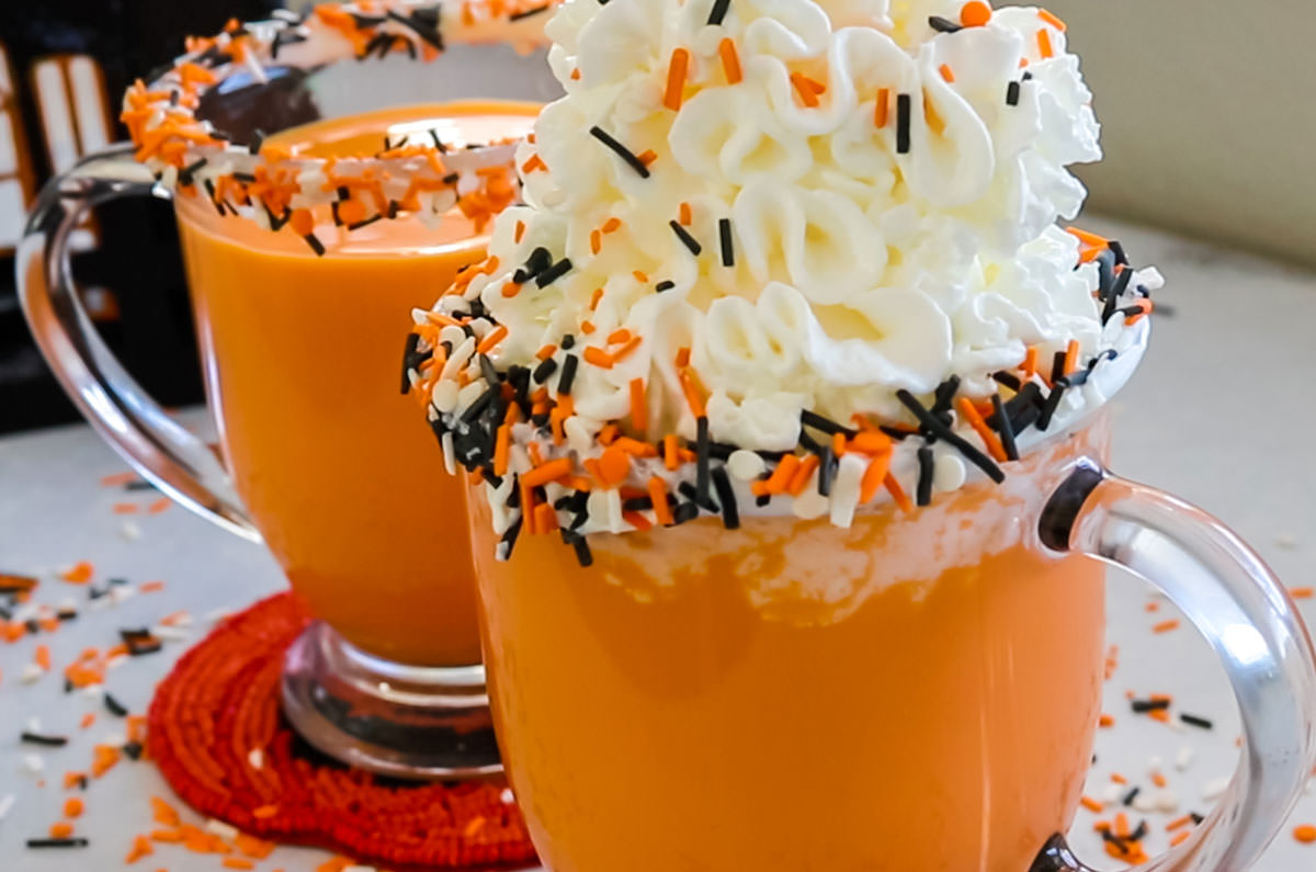 Closeup on two glasses of Halloween Hot Vanilla Milk sitting on a gray table surrounded by Halloween sprinkles.
