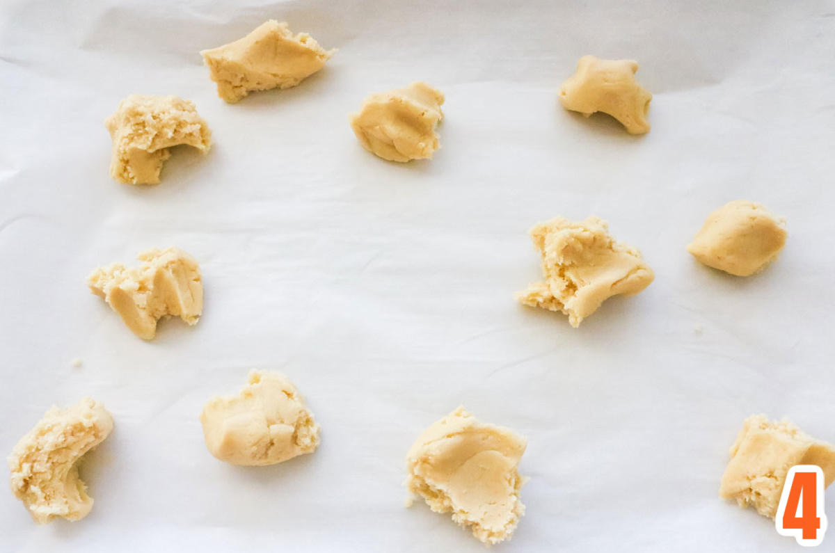 Pieces of white sugar cookie bar dough arranged on a cookie sheet covered with parchment paper.