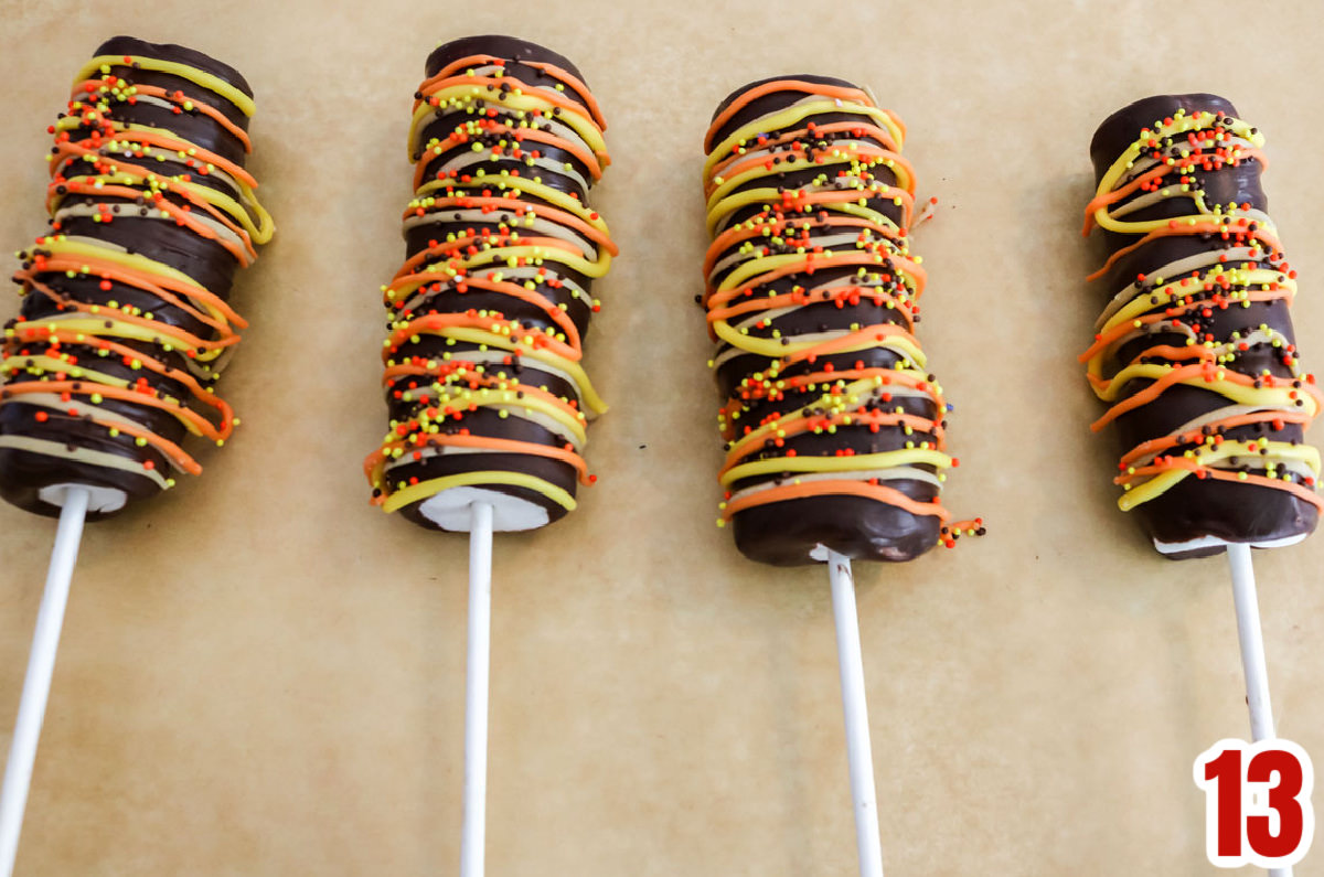 Four Harvest Marshmallow Pops laying on a piece of parchment paper.