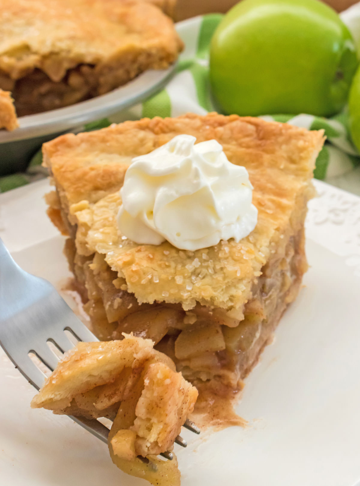 a piece of Homemade Apple Pie on a white plate with a dollop of whipped cream on top