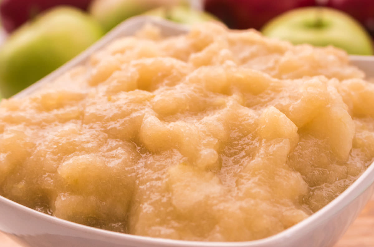 Closeup on a white bowl filled with The Best Homemade Applesauce sitting on a cutting board.