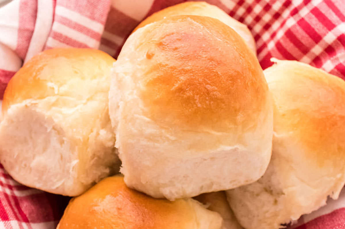 Homemade Dinner Rolls in a basket covered with a red plaid kitchen towel.