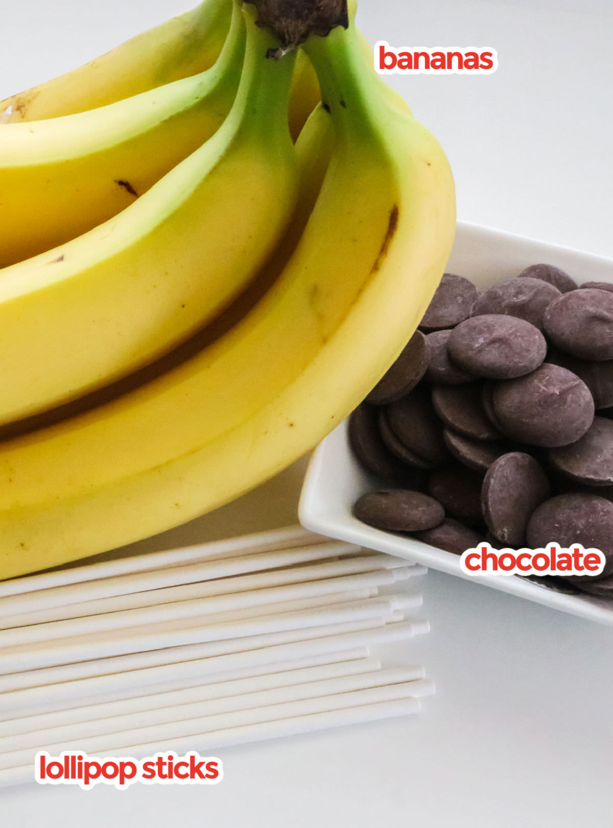 All the ingredients you will need to make a Homemade Frozen Banana including bananas, chocolate and lollipop sticks.