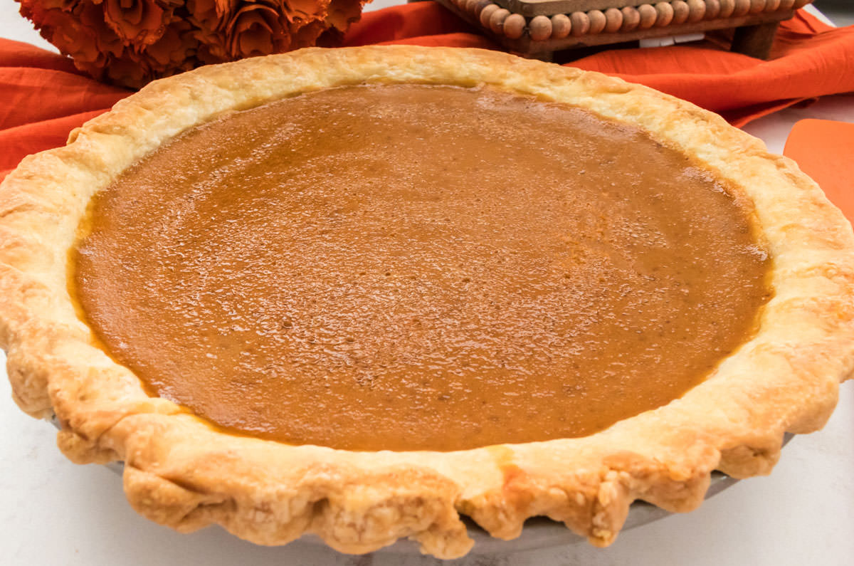 A Homemade Sweet Potato Pie sitting on a white board with a orange table linen in the background.